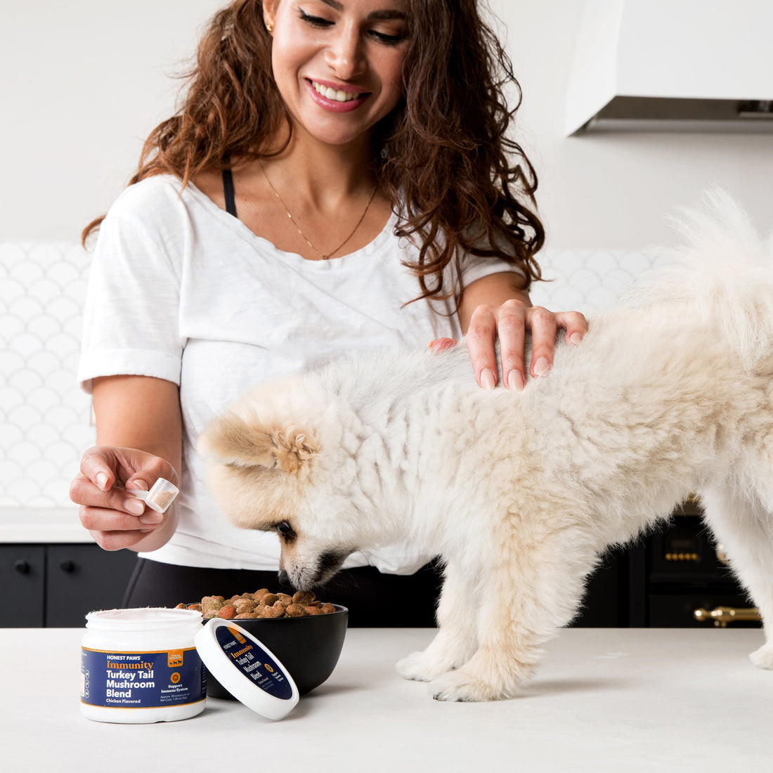 30 year old woman with brown curly hair pouring turkey tail mushroom powder on bowl of food for pomeranian